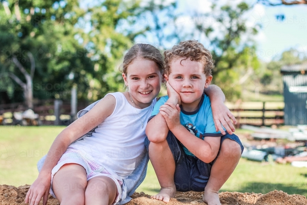 Girl with arm around boy sitting on mound of dirt - Australian Stock Image