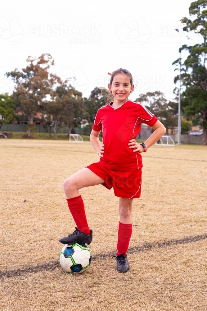 Girl with her foot on a soccer ball and hands on her hips - Australian Stock Image