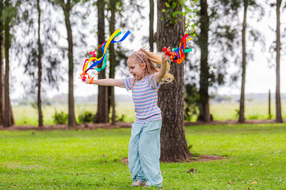 Girl with rainbow streamers running around outside in country - Australian Stock Image