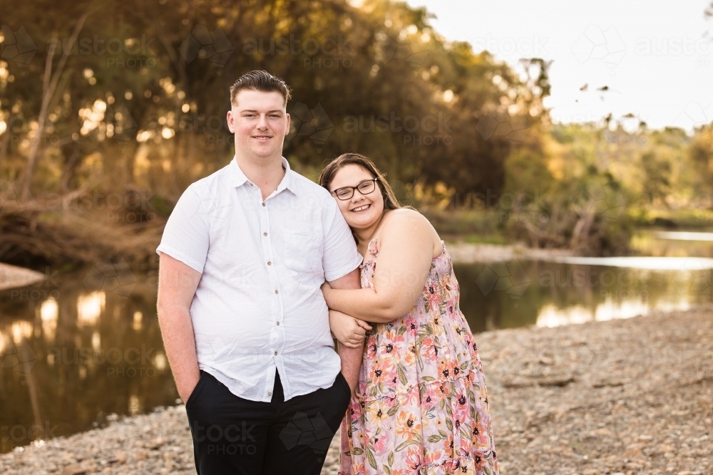 Girlfriend cuddling into boyfriends arm standing near water smiling - Australian Stock Image