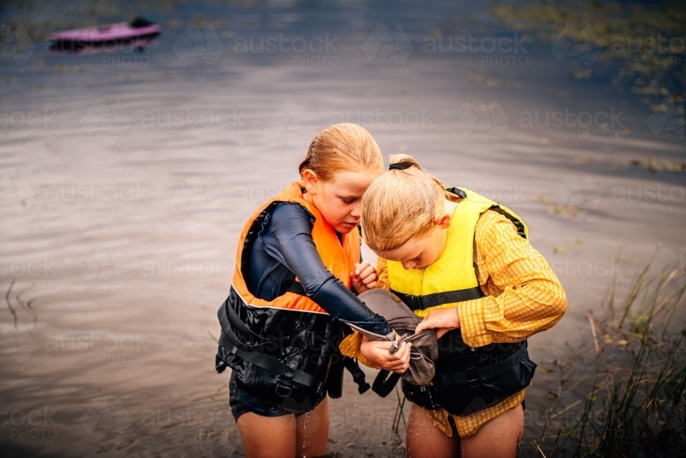 Girls looking curiously into a hat at the dam while swimingming - Australian Stock Image