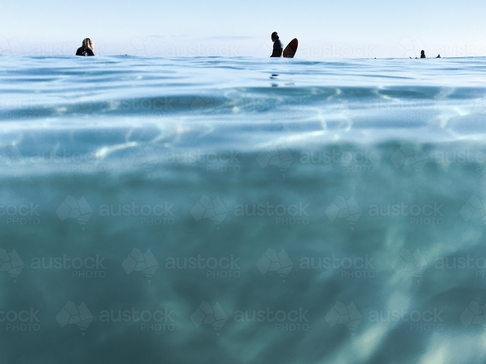 glassy blue oceans with silhouetted surfers sitting on the horizon - Australian Stock Image