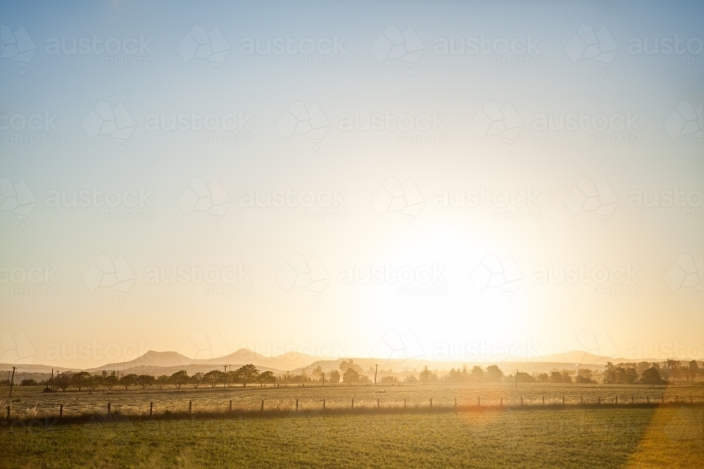 Glow of setting sun shining over farm paddock and Bulga hills - Australian Stock Image