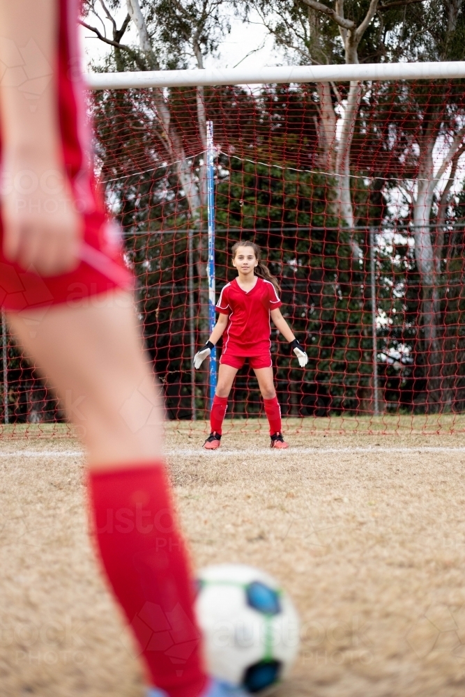 Goal keeper wearing a red football team uniform defending the goal - Australian Stock Image