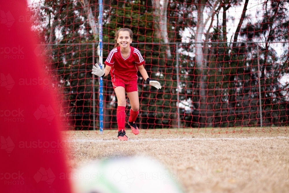 Goal keeper wearing a red football team uniform defending the goal - Australian Stock Image