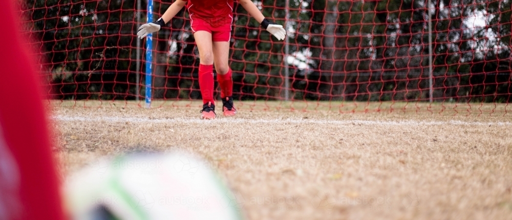 Goal keeper wearing a red football team uniform defending the goal - Australian Stock Image