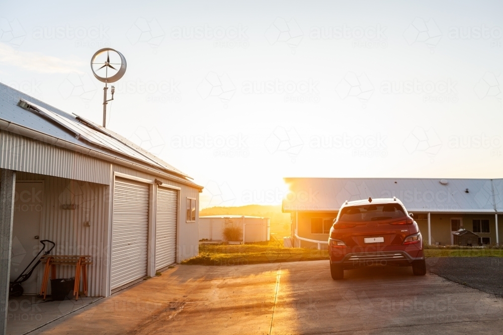 golden evening light on home wind turbine, solar panels of off grid property and electric vehicle - Australian Stock Image