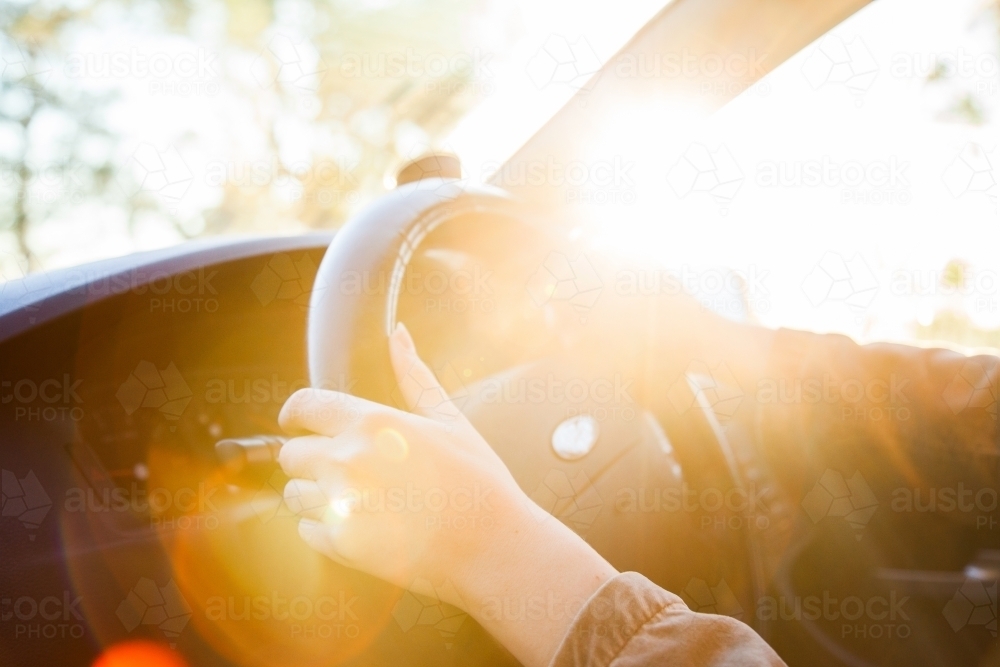 Golden sunlight flare over steering wheel and hands of car driver - Australian Stock Image