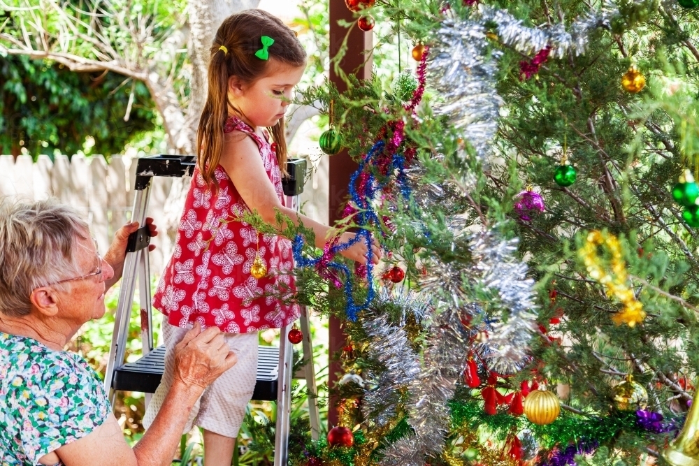 Grandchild with grandmother hanging decorations on Christmas tree - Australian Stock Image