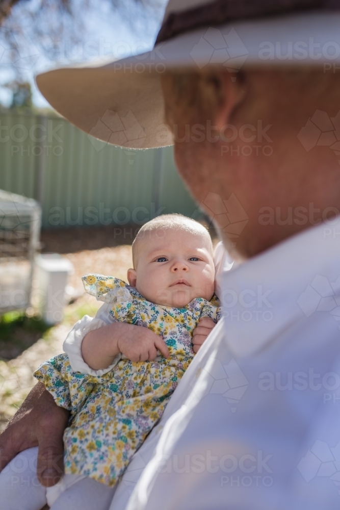 Grandfather looking down at granddaughter in arms - Australian Stock Image