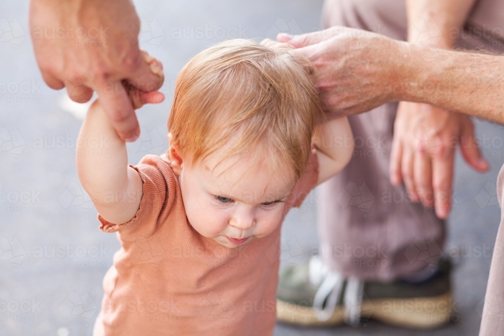 Grandfathers hand holding baby's hand helping baby to walk - Australian Stock Image