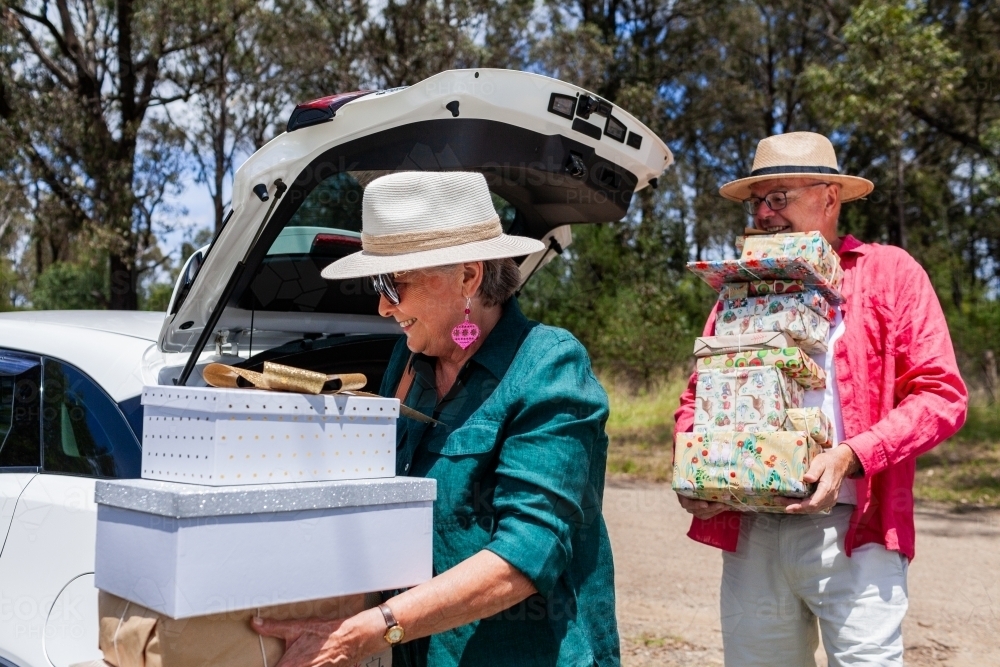 Grandmother and grandfather unpacking piles of Christmas gifts from car boot at Christmastime - Australian Stock Image
