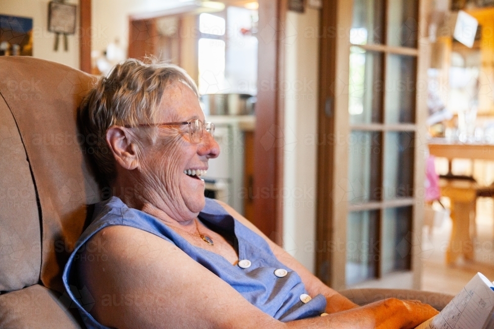 Grandmother sitting in chair inside laughing - Australian Stock Image