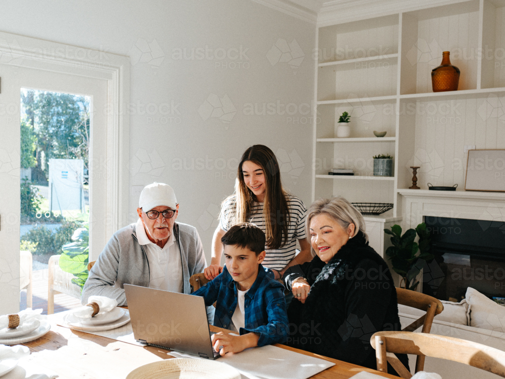 Grandparents sitting with their grandchildren in front of a laptop on the table. - Australian Stock Image