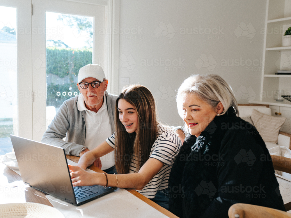 Grandparents sitting with their granddaughter in front of a laptop on the table. - Australian Stock Image