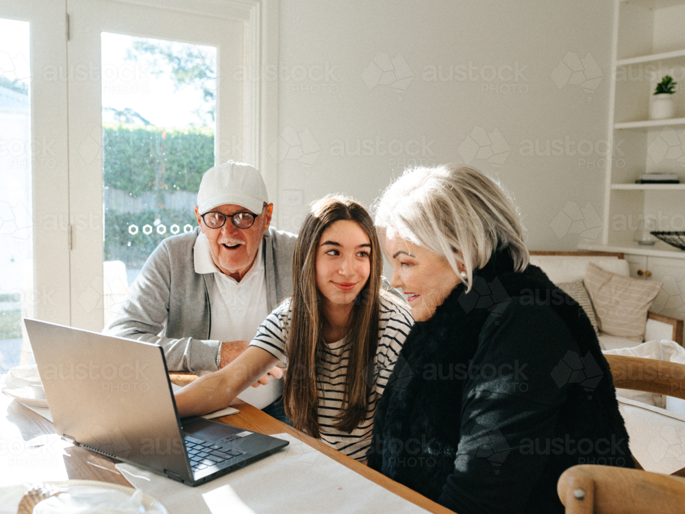 Grandparents sitting with their granddaughter in front of a laptop on the table. - Australian Stock Image