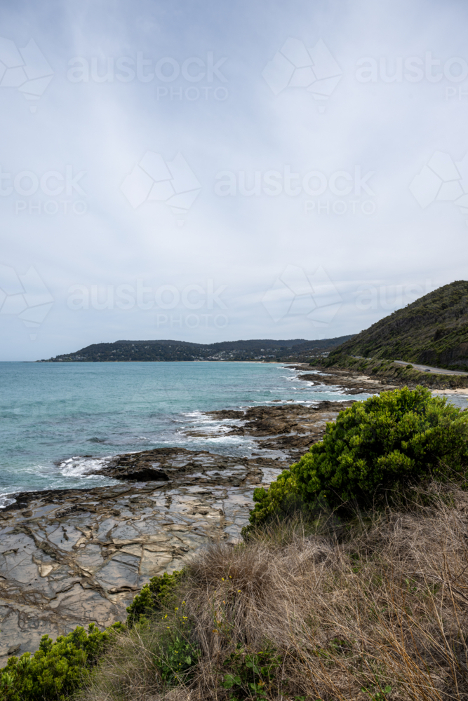 Great Ocean Road scenery with ocean coming to rocky shore under overcast sky - Australian Stock Image