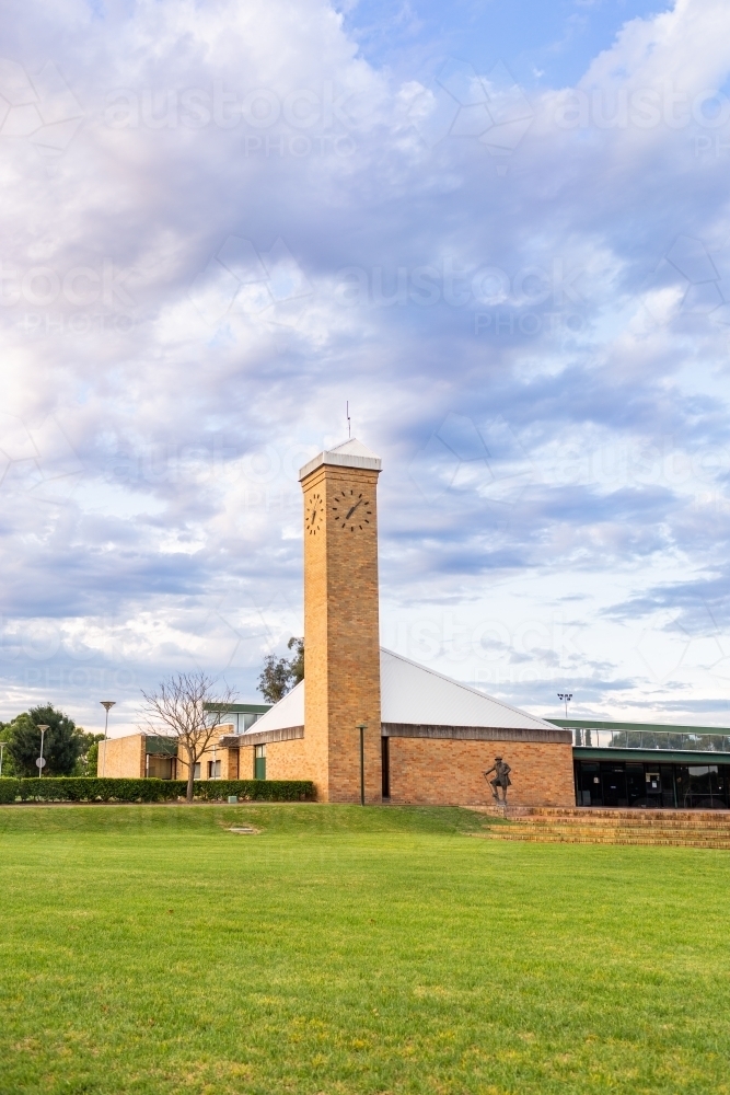 Green lawn to brick buildings and clock tower in town at dusk - Australian Stock Image