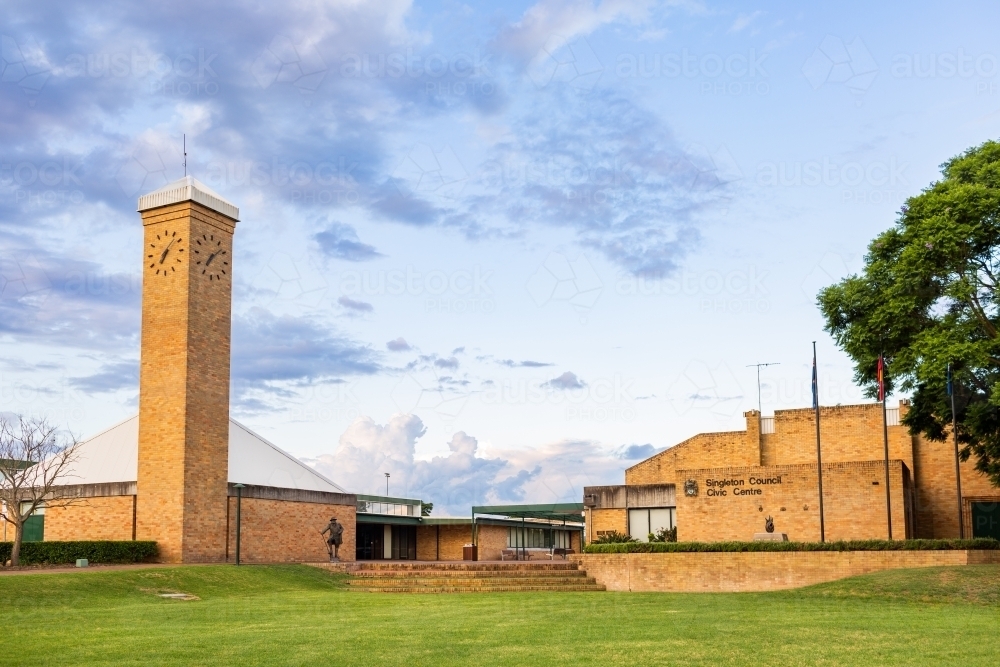 Green lawn to brick buildings and clock tower in town at dusk - Australian Stock Image