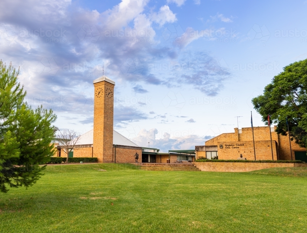 Green lawn to brick buildings and clock tower in town at dusk - Australian Stock Image