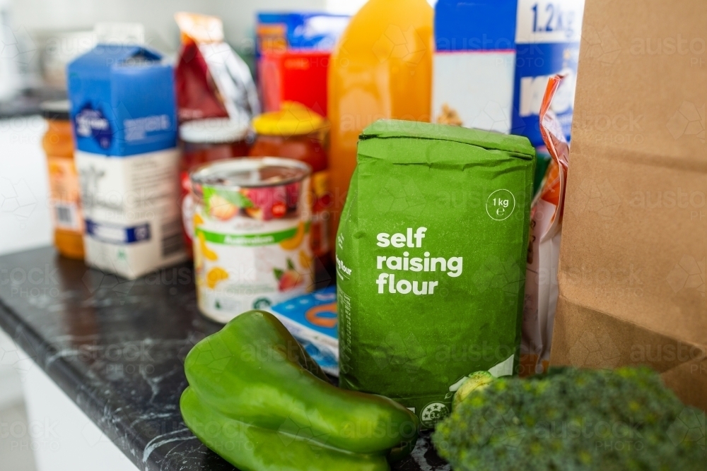 green vegetables, self raising flour and other grocery shopping sitting on kitchen bench - Australian Stock Image