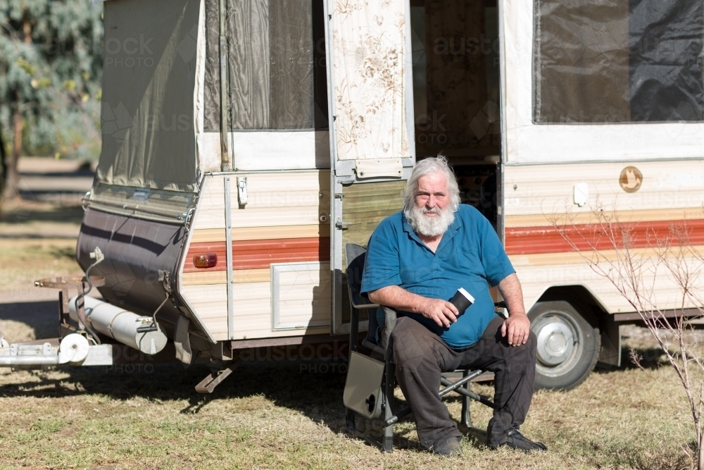 Grey haired man sitting in front of pop-up caravan - Australian Stock Image