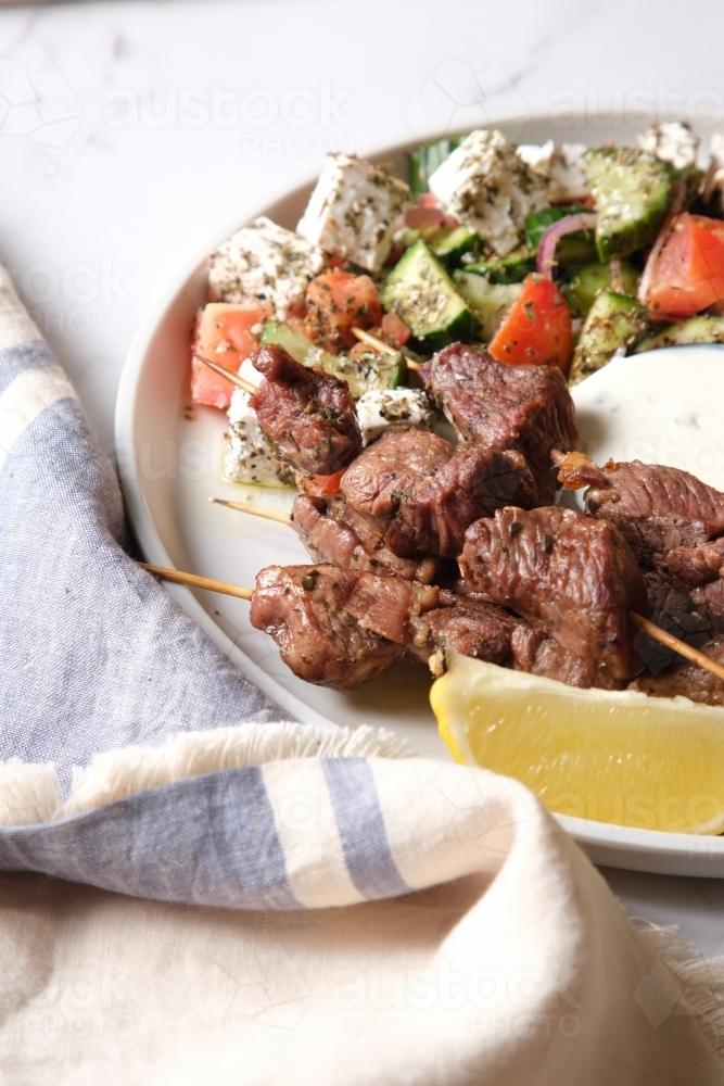 Grilled meat served on a white plate with fries, white sauce, vegetable salad, and pita bread - Australian Stock Image