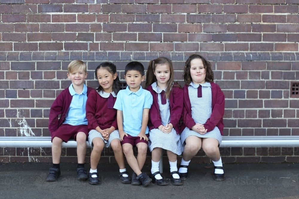 Group of kids sitting together on a school bench outside - Australian Stock Image