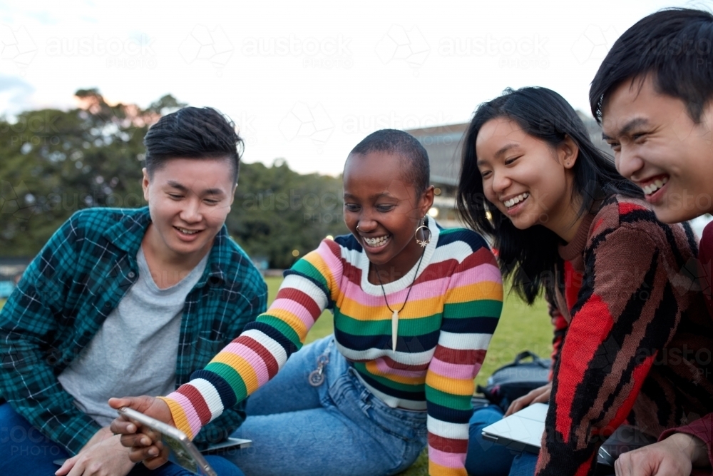 Group of young university students hanging out sitting on grass studying and using devices - Australian Stock Image