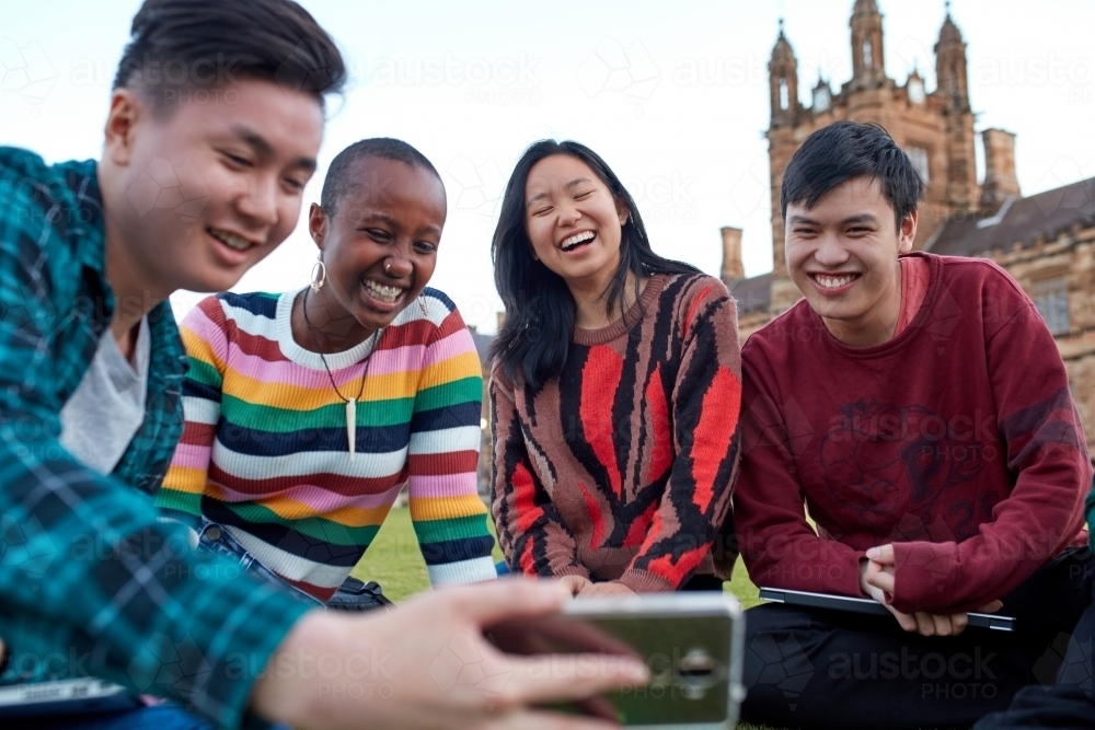 Group of young university students hanging out sitting on grass studying and using devices - Australian Stock Image