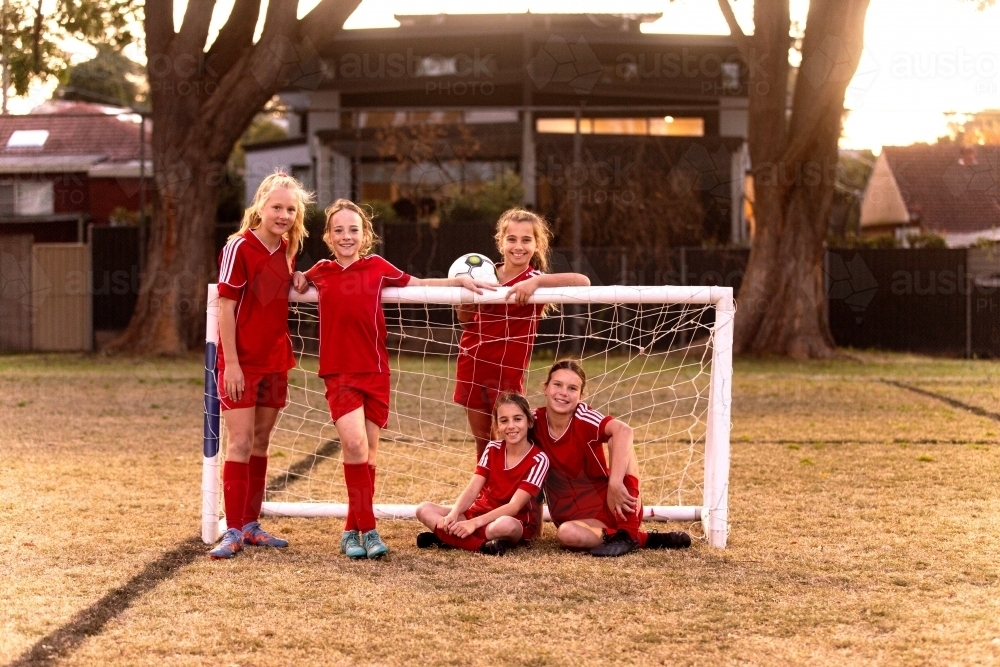 Group portrait of a tween girls football team leaning against small goal posts - Australian Stock Image