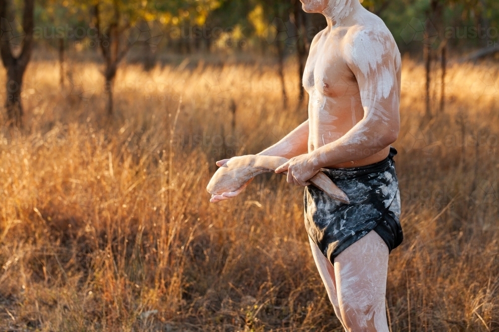 Half body shot of aboriginal australian in cultural ochre body paint holding stick - Australian Stock Image