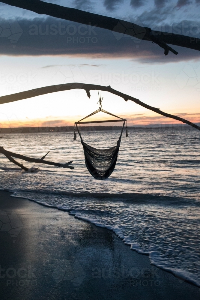 Hammock hanging from a tree branch on a beach at sunset - Australian Stock Image