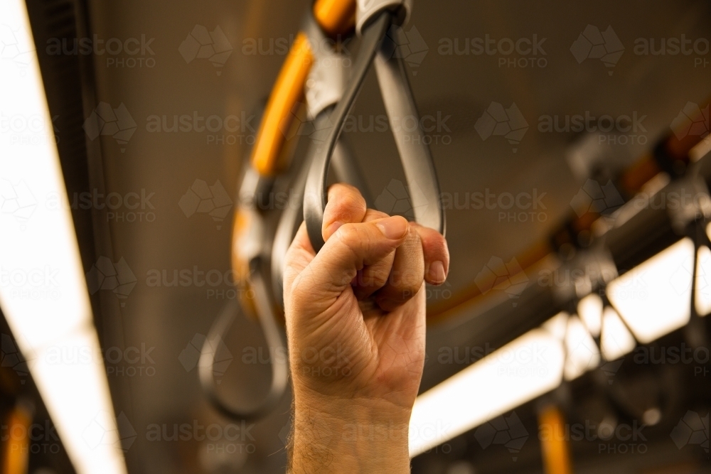 hand holding a loop handle from the ceiling of a train - Australian Stock Image