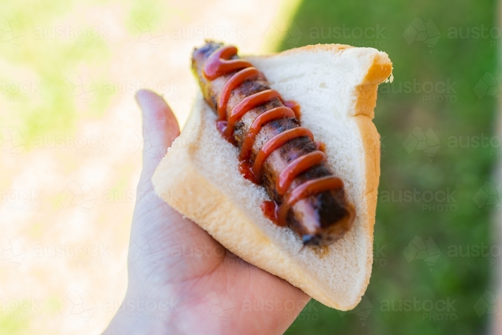 hand holding bbq sausage with sauce in white bread - Australian Stock Image
