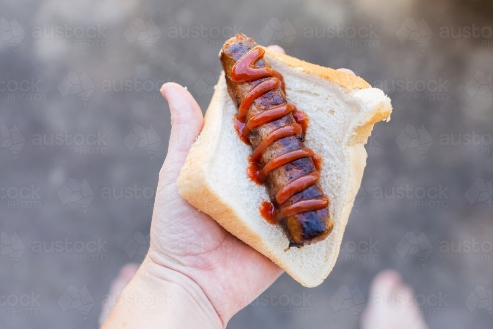 hand holding bbq sausage with sauce in white bread - Australian Stock Image