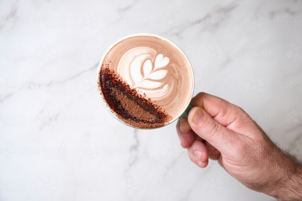 Hand holding hot chocolate over marble surface - Australian Stock Image