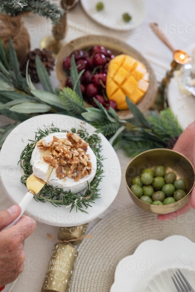 Hand lifting slice of camembert cheese at Christmas-decorated table - Australian Stock Image