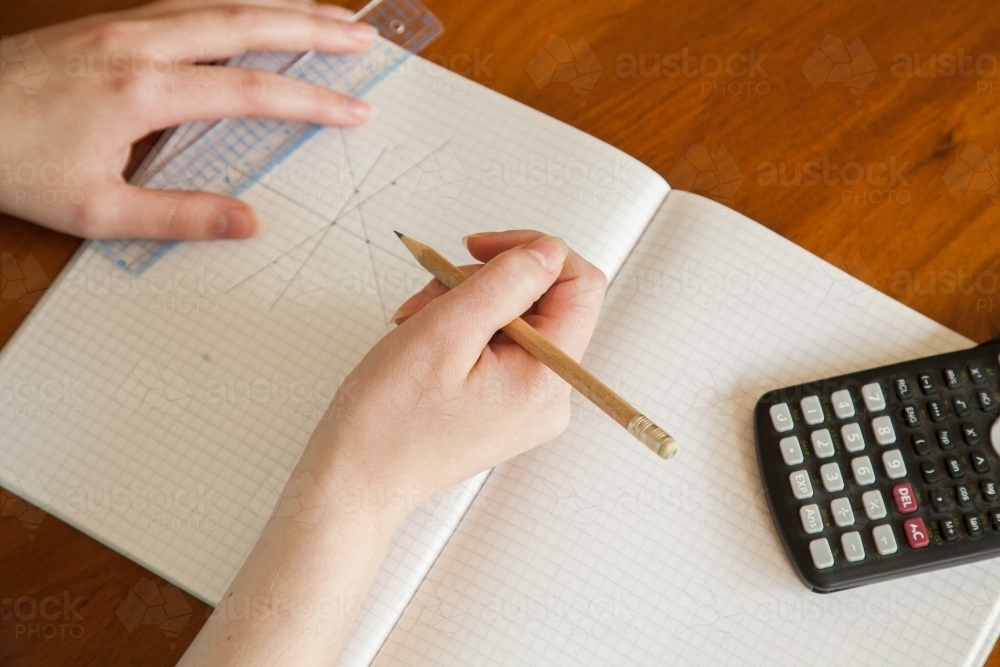 Hands drawing out maths problem on graph paper - Australian Stock Image