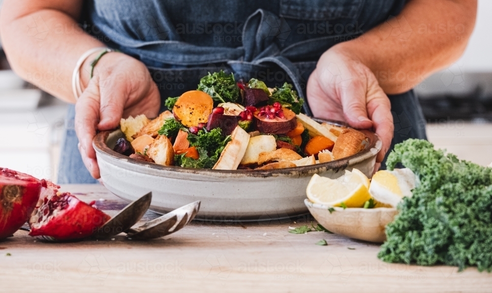 Hands holding a salad bowl on kitchen bench. - Australian Stock Image