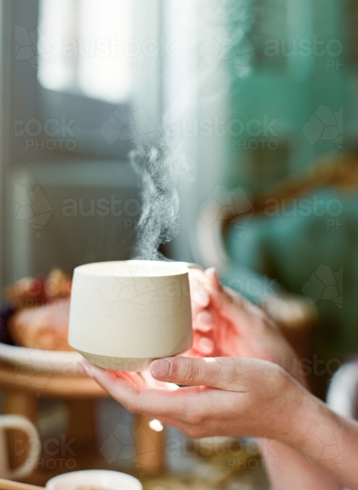 Delicate Hands holding a warm cup of tea with steam - Australian Stock Image