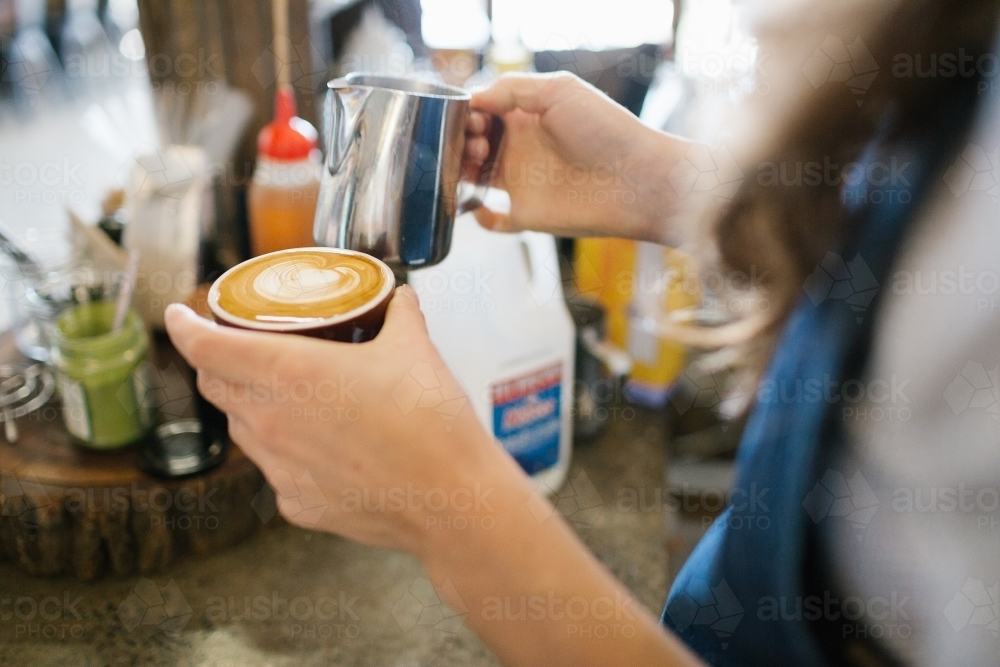 Hands of barista holding milk jug and coffee - Australian Stock Image