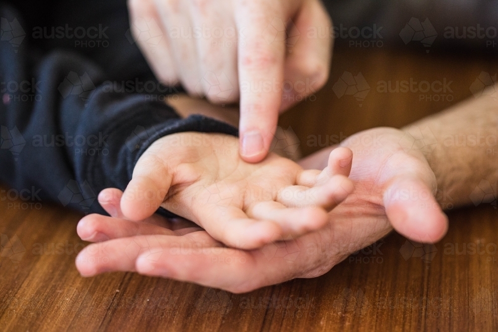 Hands of man tracing lines on child's hand - Australian Stock Image