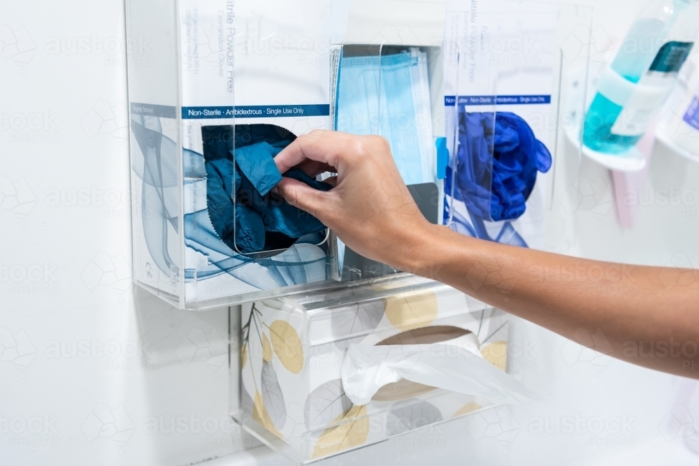 Hands removing disposable gloves from a box - Australian Stock Image