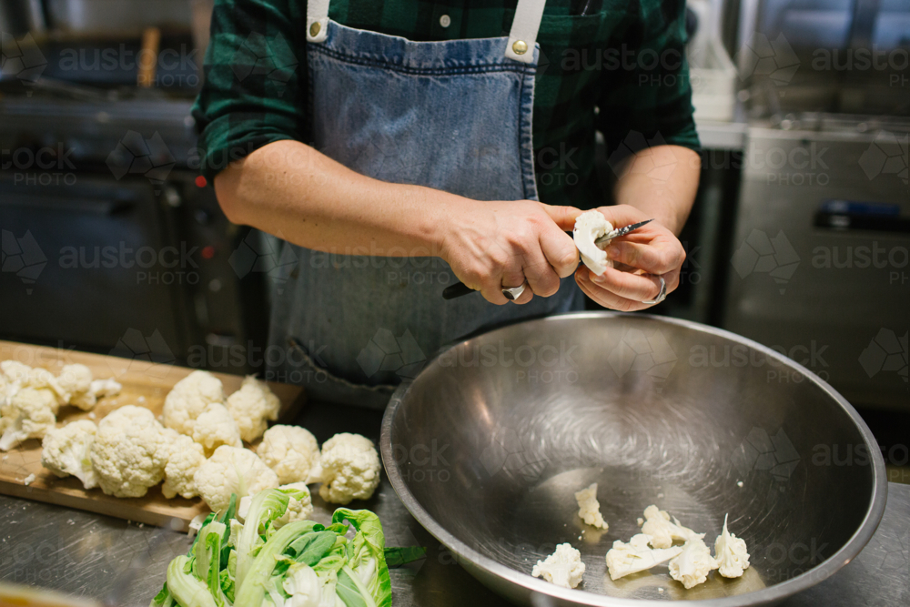 Hands slicing cauliflower in kitchen over metal bowl - Australian Stock Image