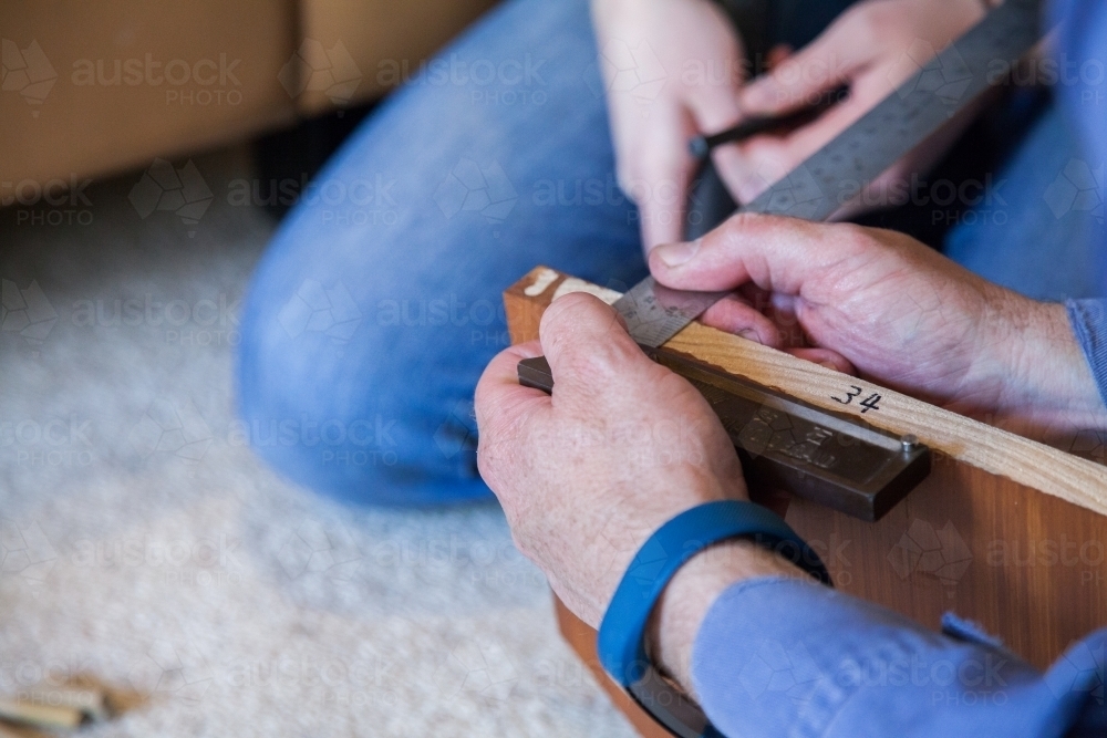 Hands with tools measuring where to make cut in piece of wood - Australian Stock Image