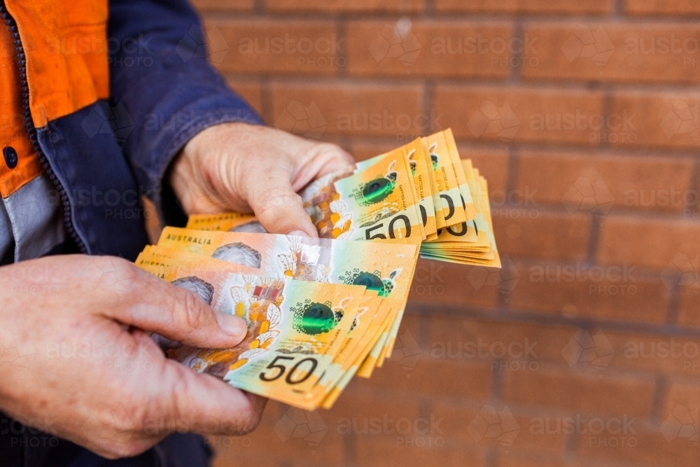 Handyman holding bank notes counting cash received as payment for job completion - Australian Stock Image