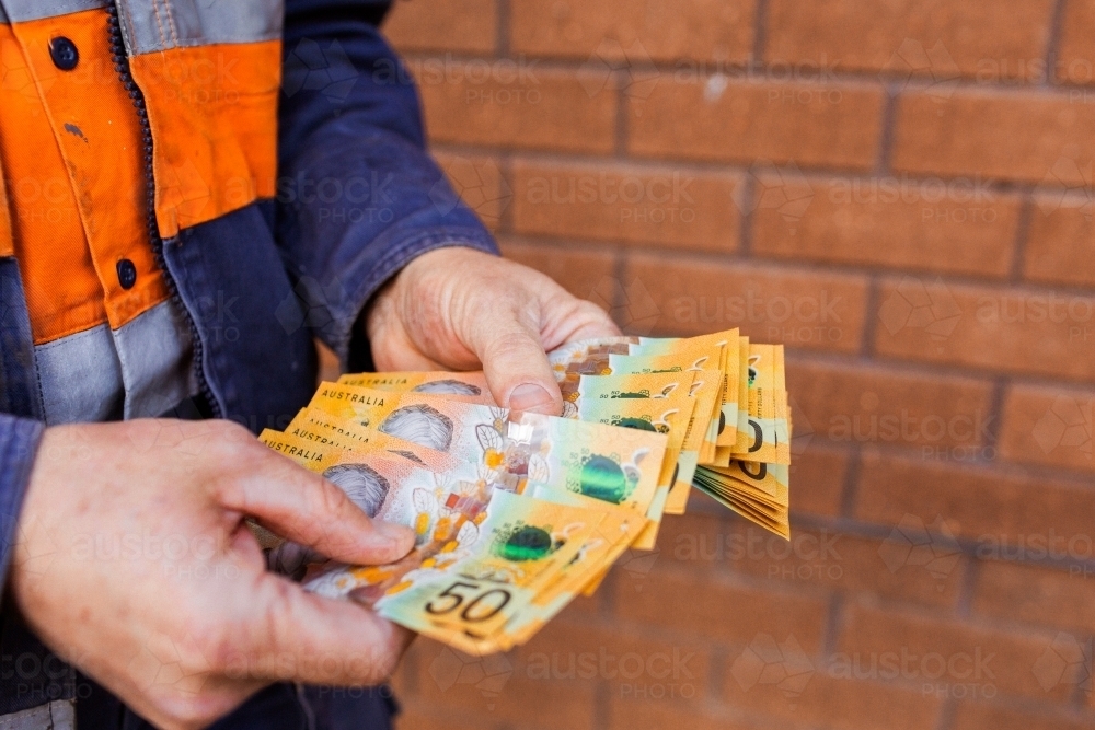 Handyman holding bank notes counting cash received as payment for job completion - Australian Stock Image