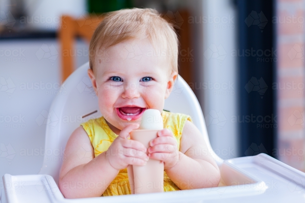 happy 9 month old baby in high chair eating milk ice-block during hot summers day - Australian Stock Image