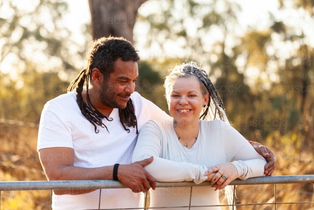 Happy aboriginal Australian couple leaning on farm gate together in country - Australian Stock Image